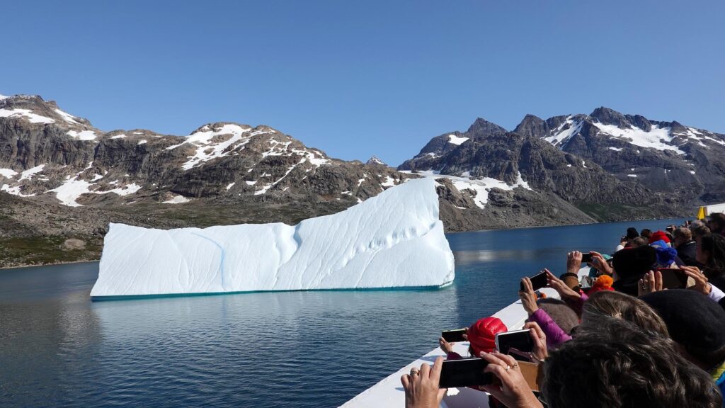 Tourists take pictures of an iceberg with their phones.