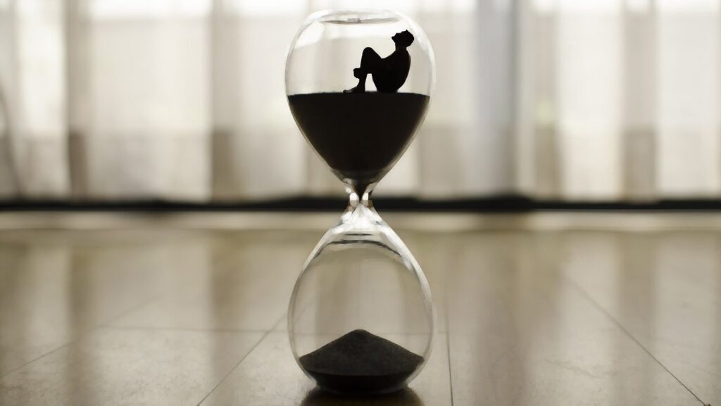 The silhouette of a man appears to sit on top of sand in an hourglass.